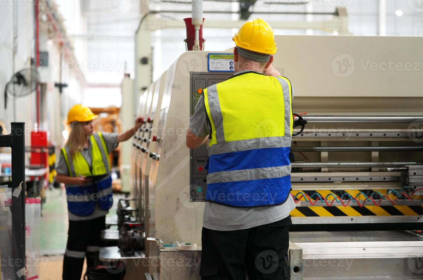 Two workers in safety vests and hard hats working on a machine photo