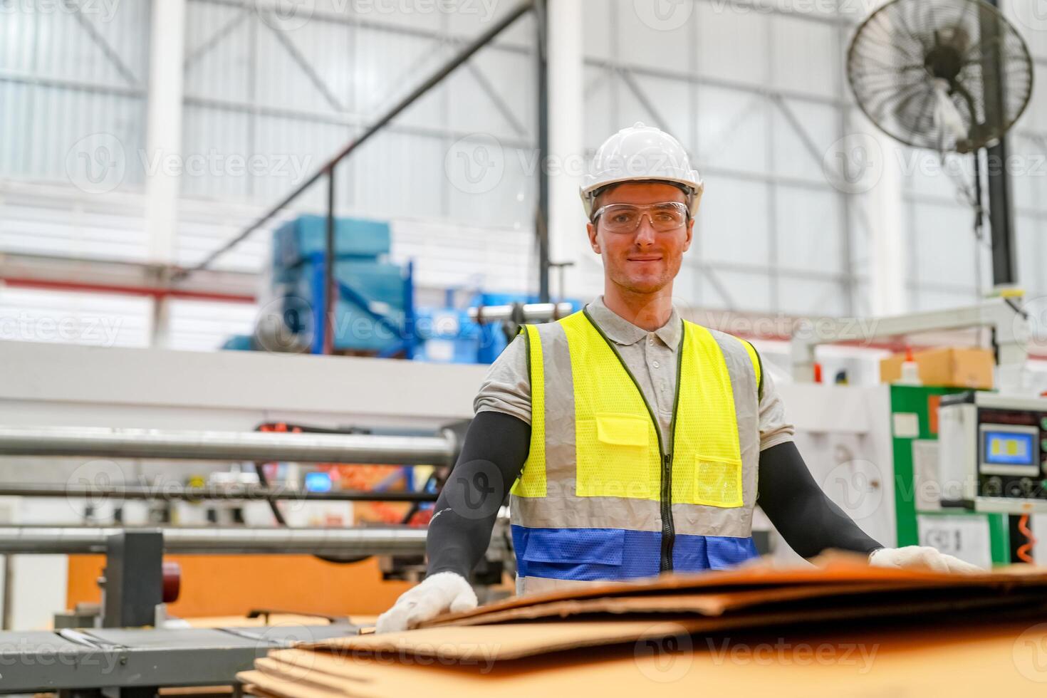 A man in a safety vest standing in front of a large stack of cardboard photo