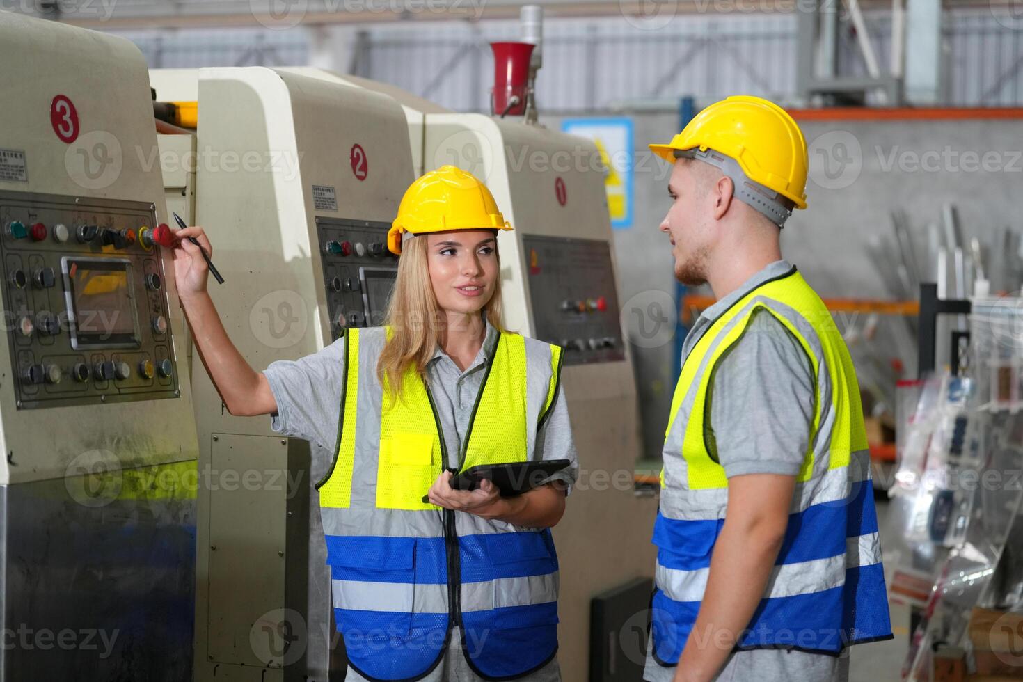 Two people in safety vests standing next to a machine photo