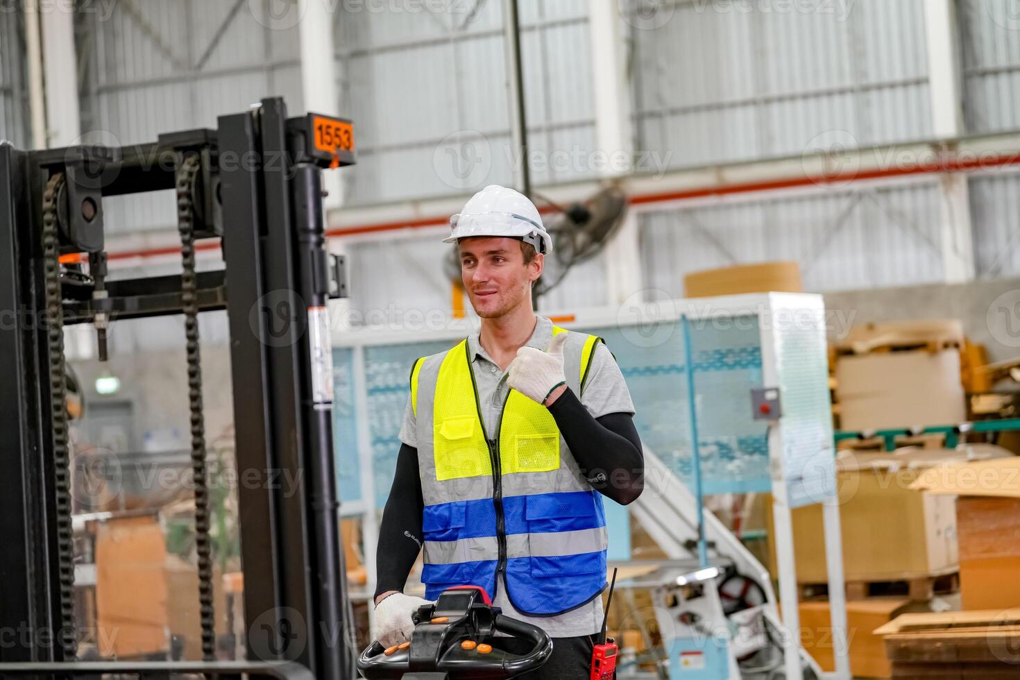 A man in a safety vest standing next to a forklift photo