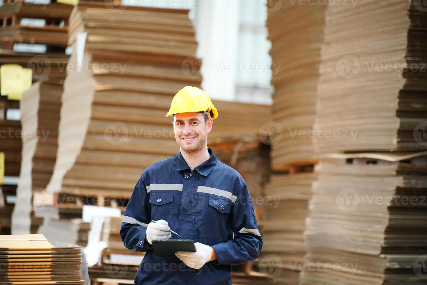 A smiling man in a hard hat standing in front of stacks of cardboard boxes photo
