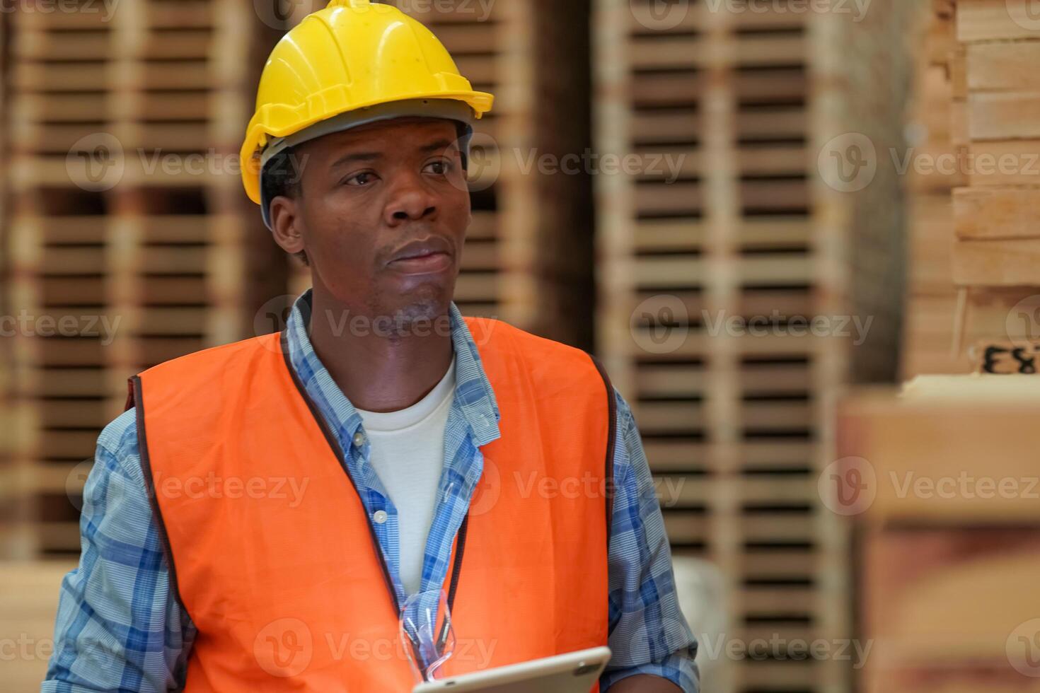 A man in an orange vest and hard hat standing in front of stacks of wooden pallets photo