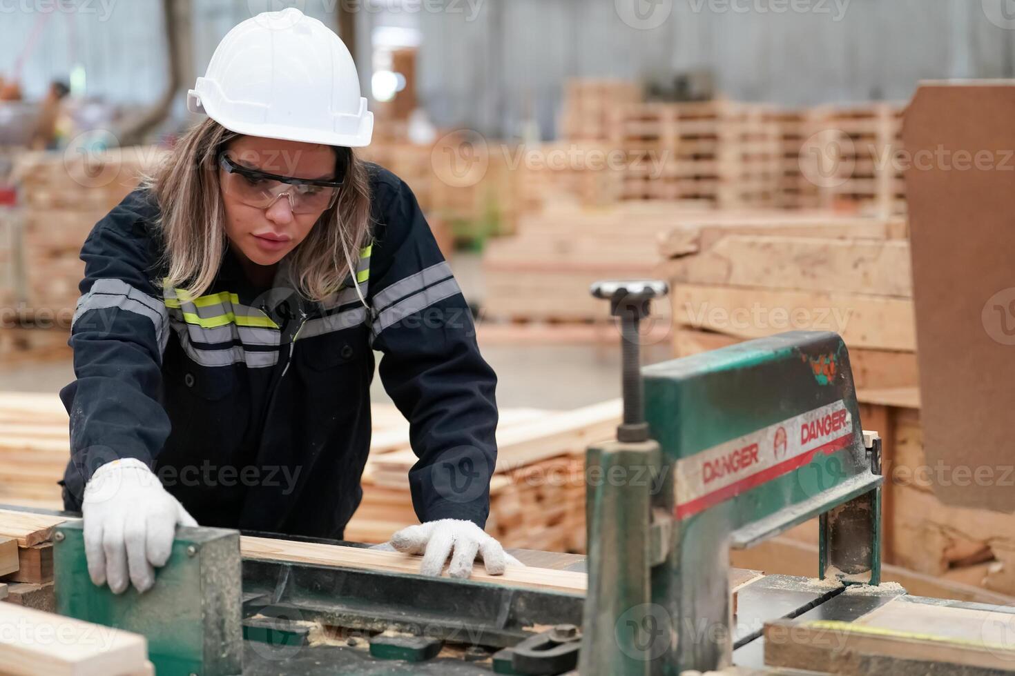 A woman in a hard hat and safety glasses working on a piece of wood photo