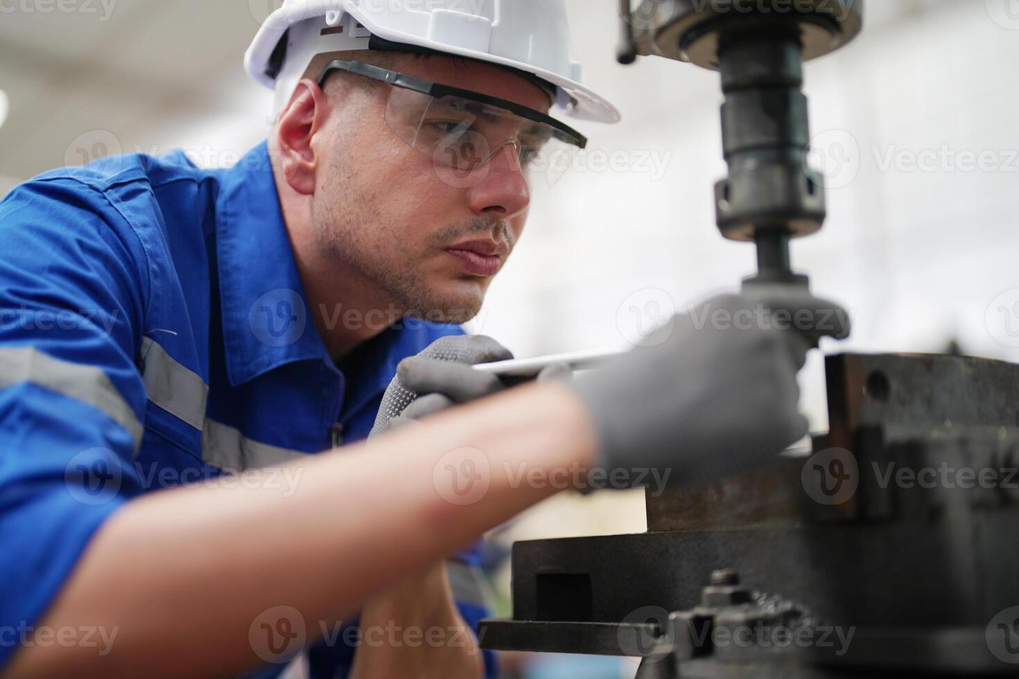 A man in a blue shirt and hard hat working on a machine photo