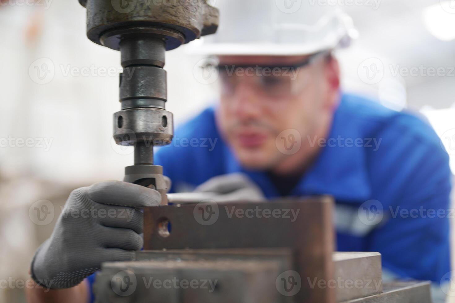 A man in a blue shirt and white helmet is working on a machine photo