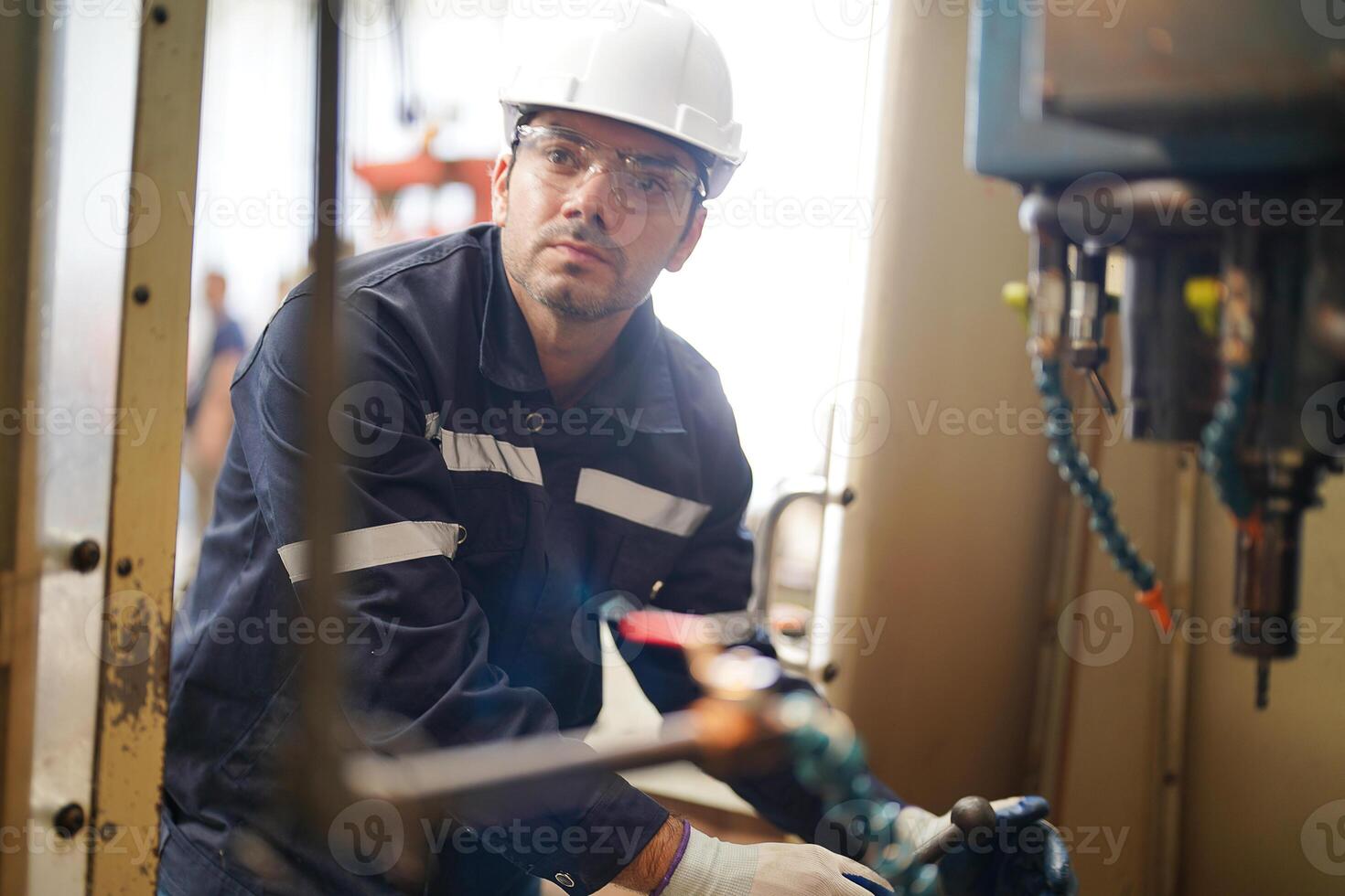A man in a hard hat and safety glasses working on a machine photo