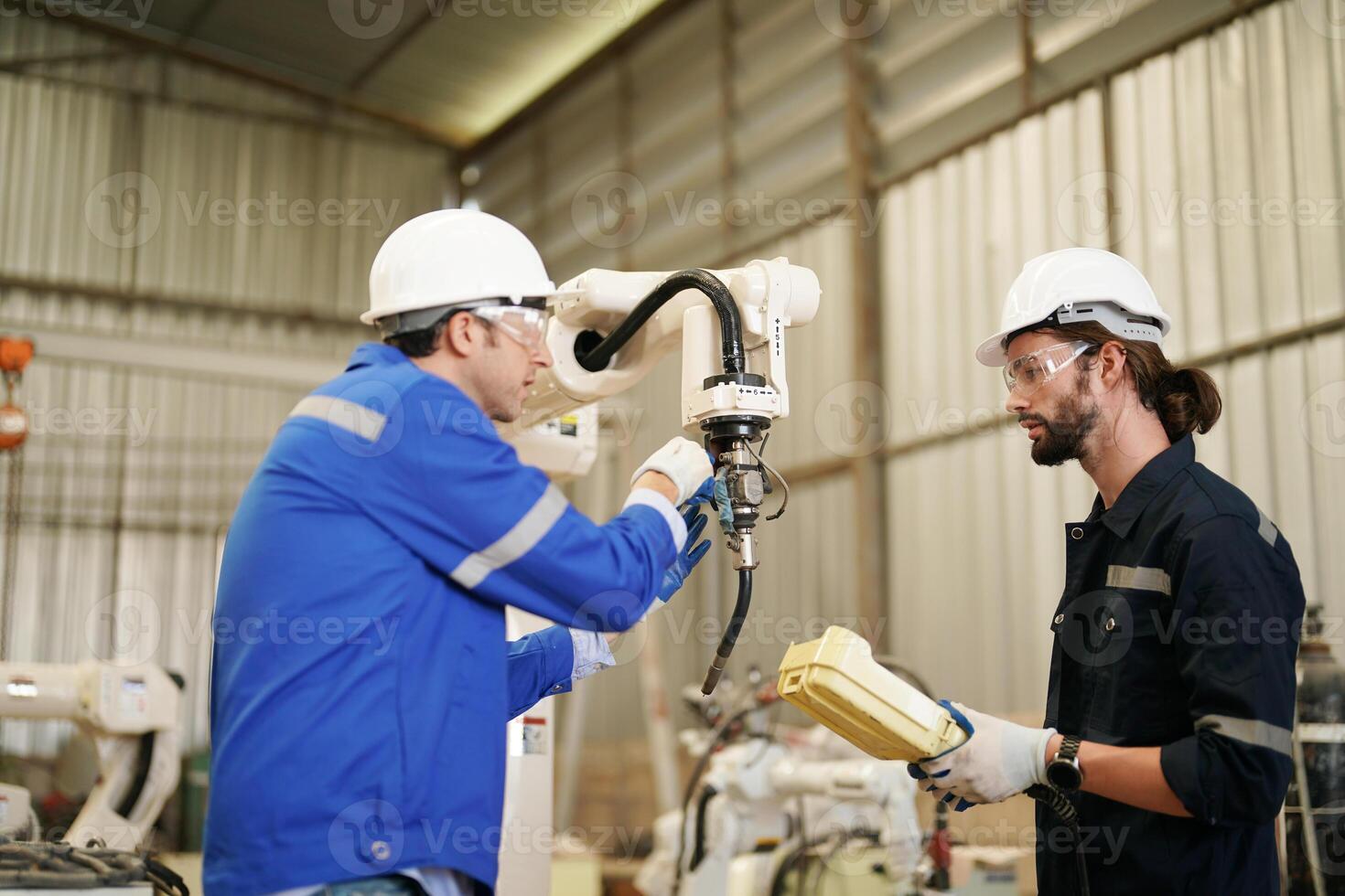 Two men in blue overalls working on a machine photo