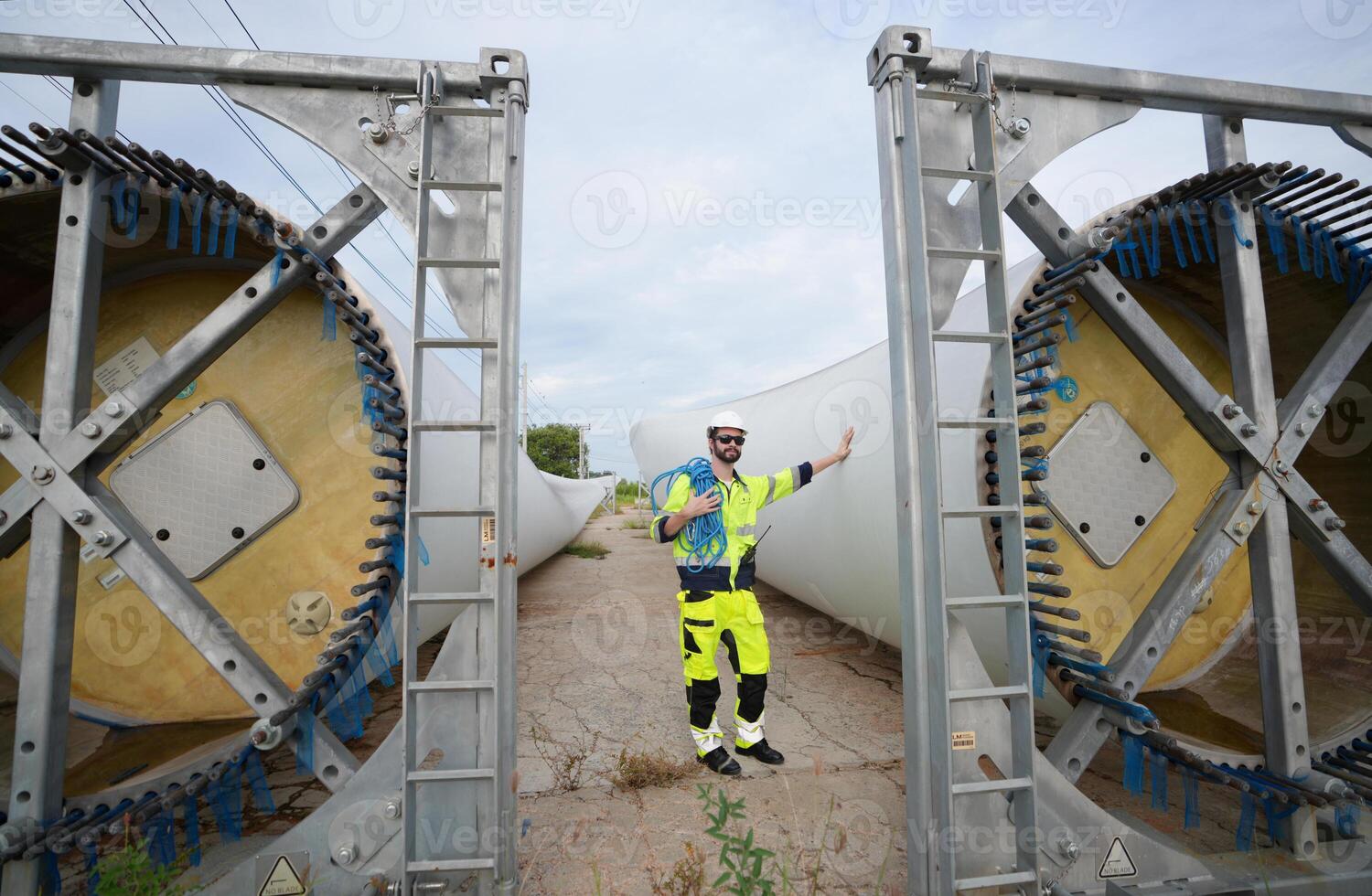 A man in yellow safety gear standing next to some large wind turbines photo