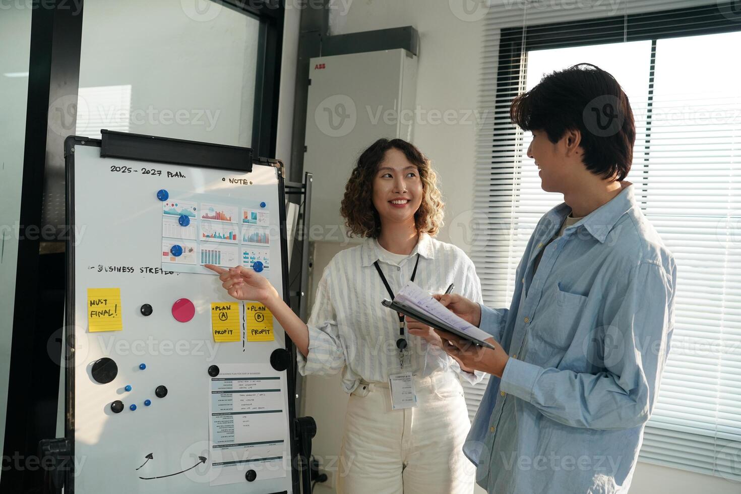 A man and woman standing in front of a white board photo