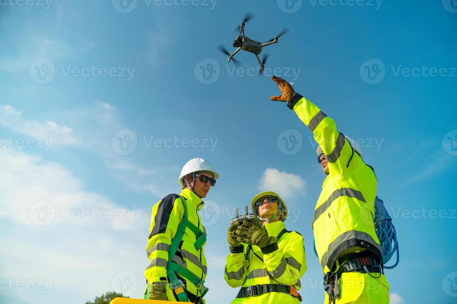 Three men in yellow safety gear are holding up a drone photo