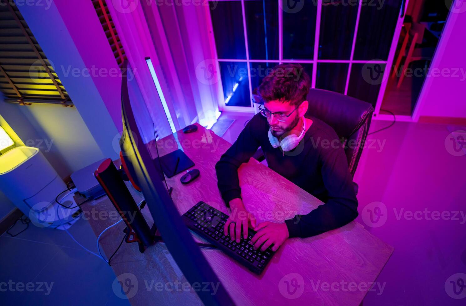 A man sitting at a desk with a computer and a purple light photo