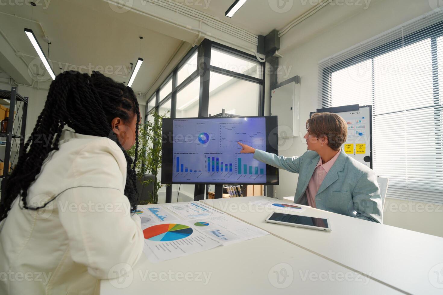 Two people sitting at a table with a large screen photo