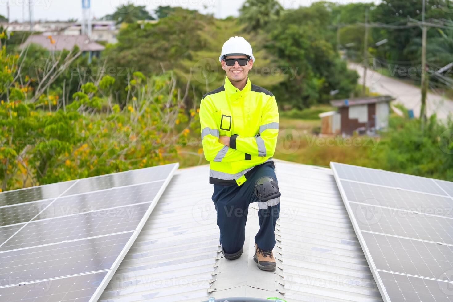 A man in a safety vest and hard hat sitting on top of a solar panel photo