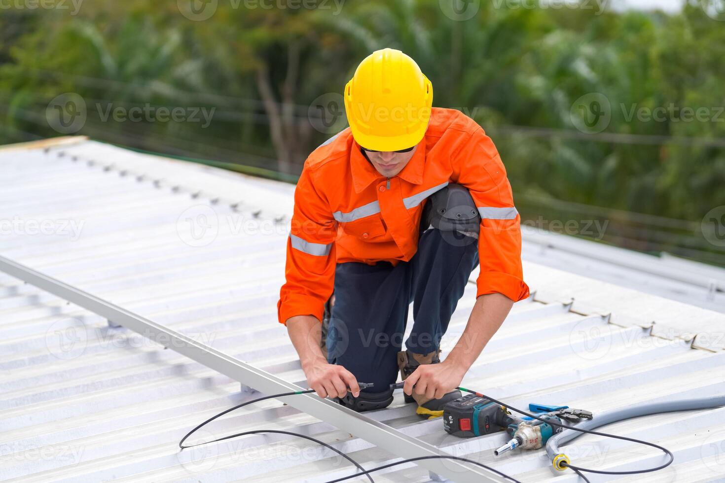 A man in an orange shirt and hard hat working on a roof photo