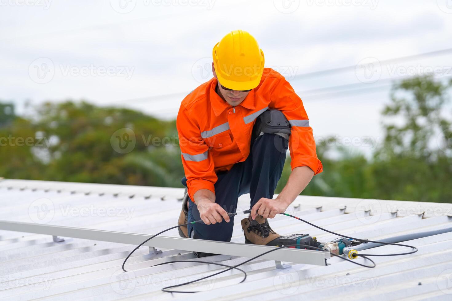 A man in an orange shirt and hard hat working on a solar panel photo