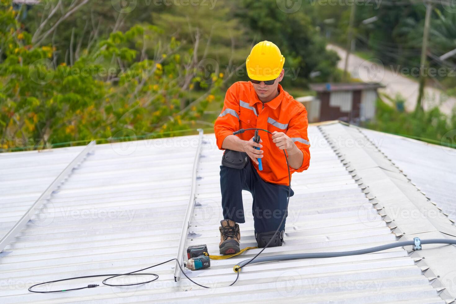 A man in an orange shirt and hard hat on a roof photo