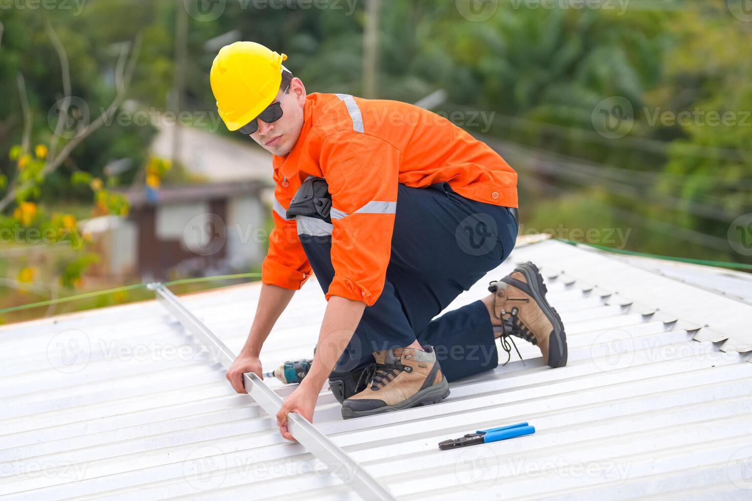A man in an orange shirt and hard hat working on a roof photo