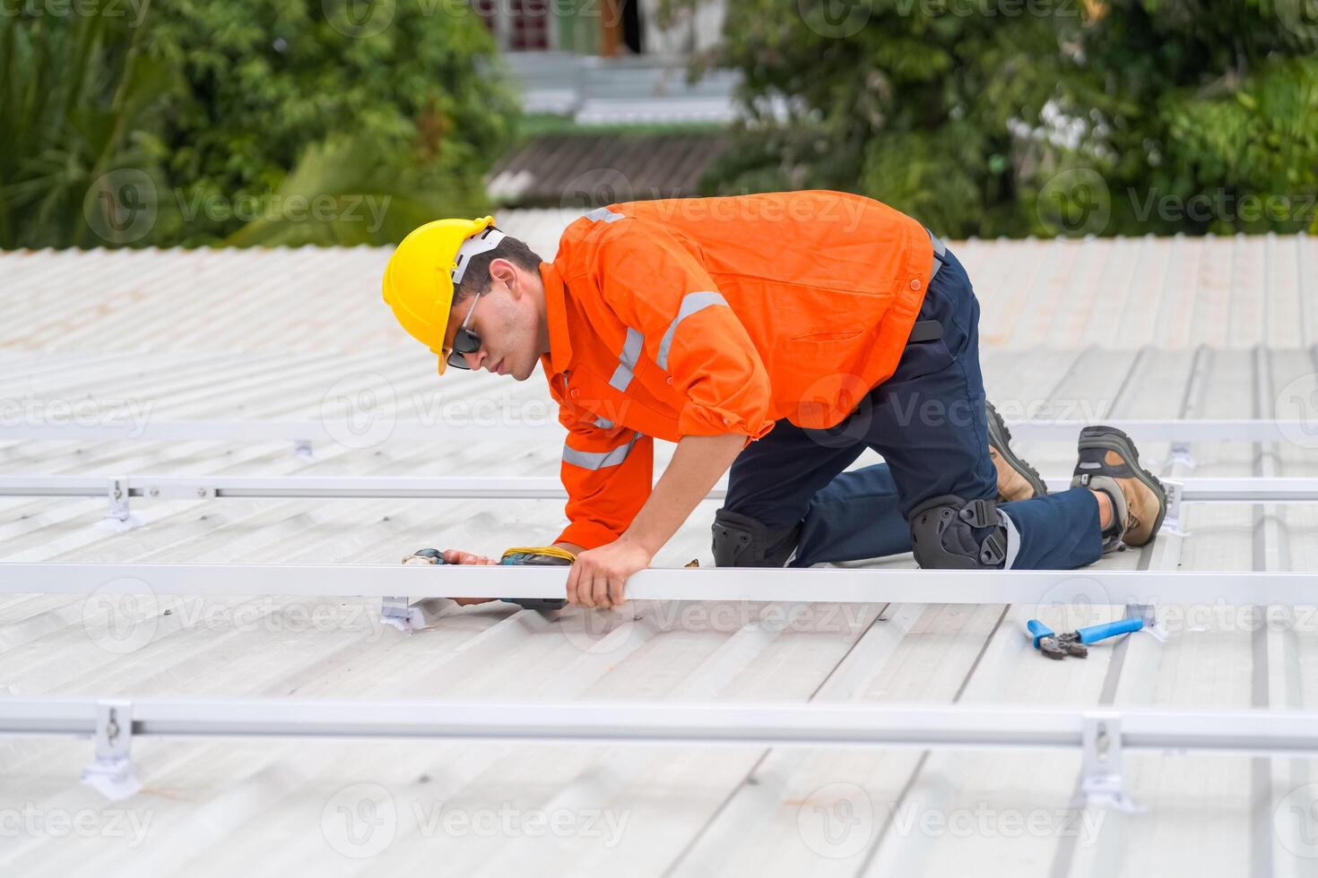 A man in an orange shirt and safety vest working on a roof photo