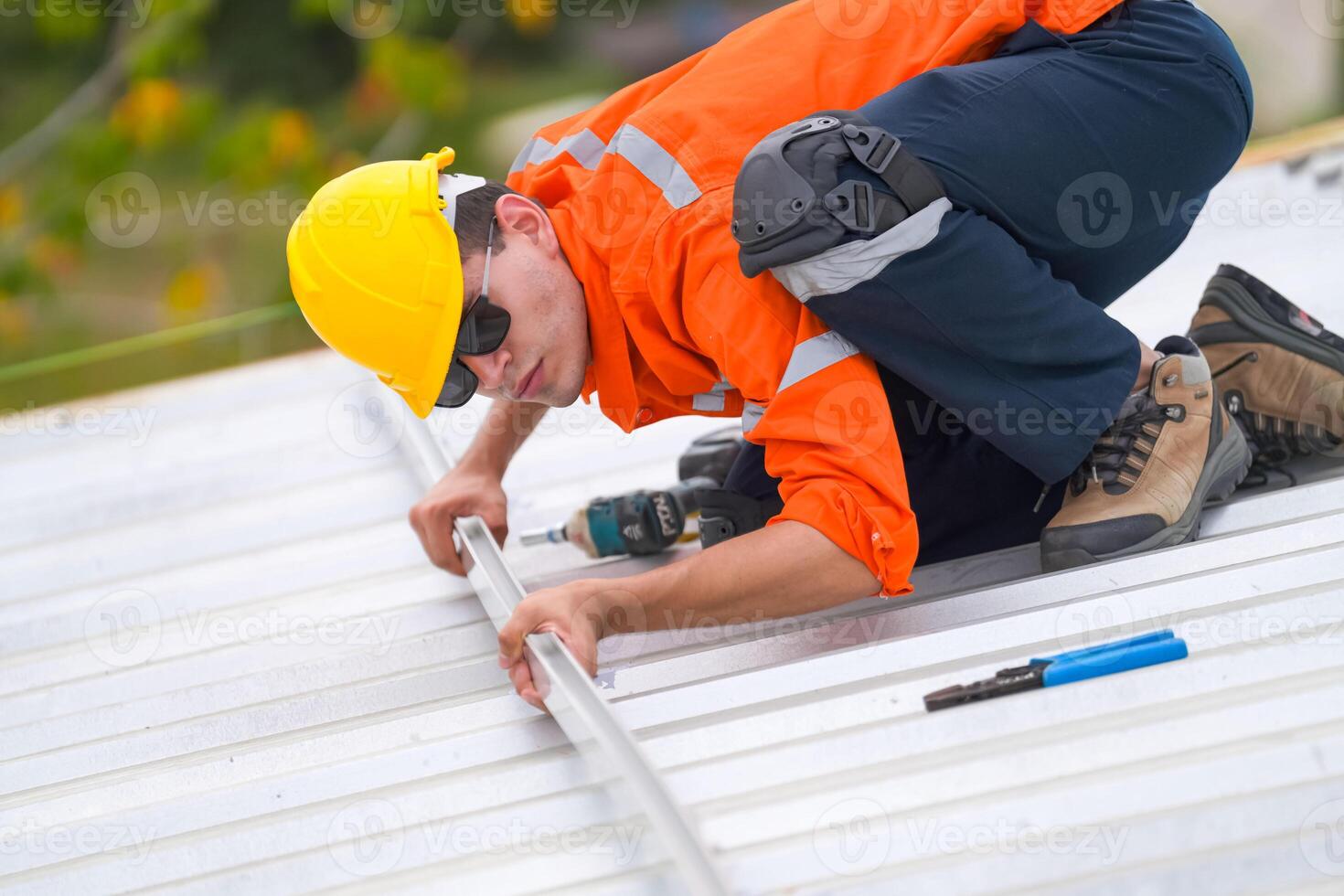 A man in an orange shirt and hard hat working on a roof photo