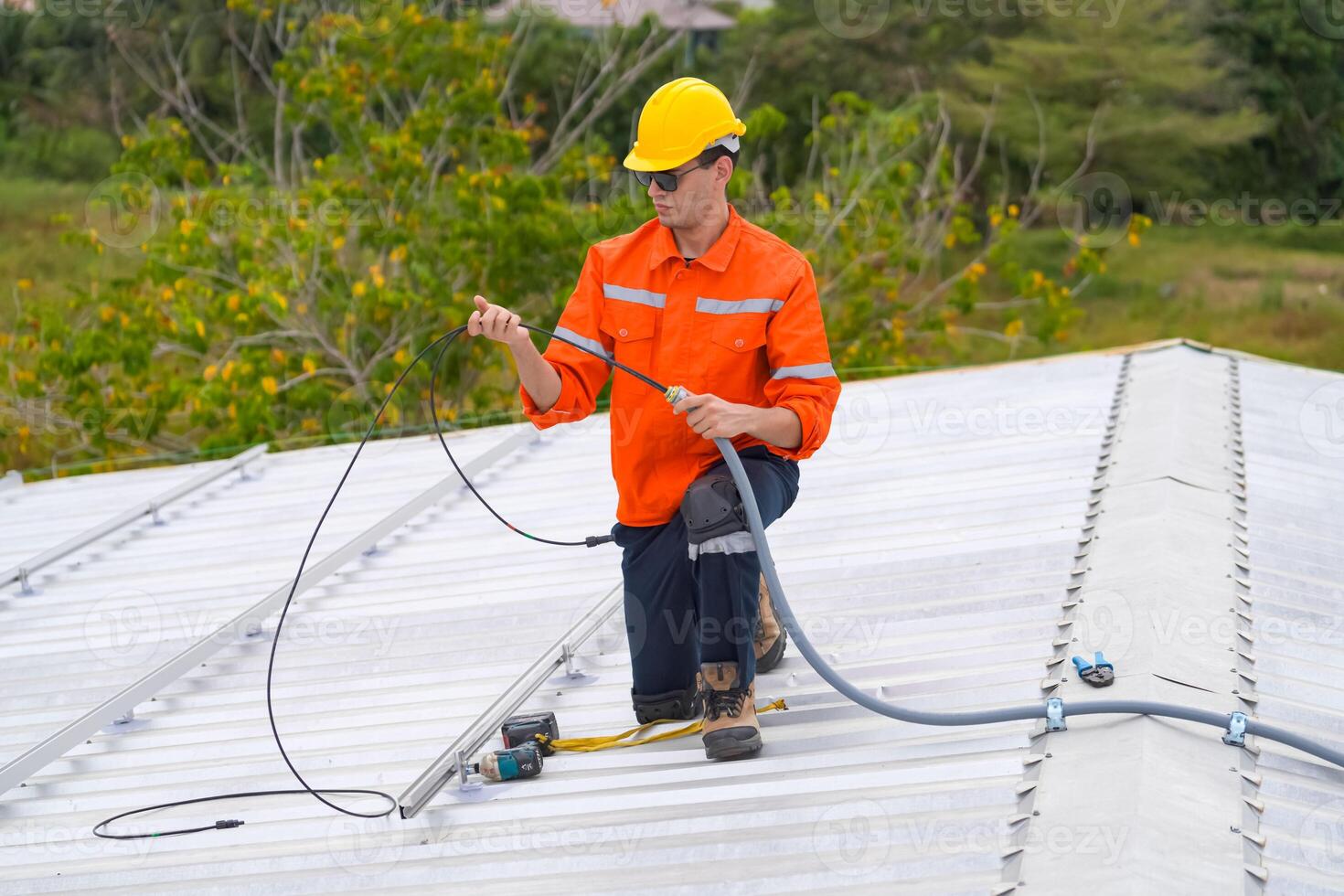 A man in an orange shirt and hard hat is working on a roof photo