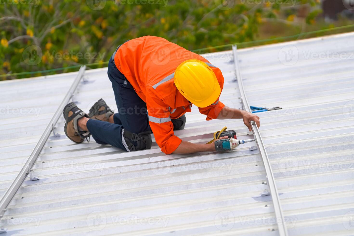 A man in an orange shirt and hard hat working on a roof photo