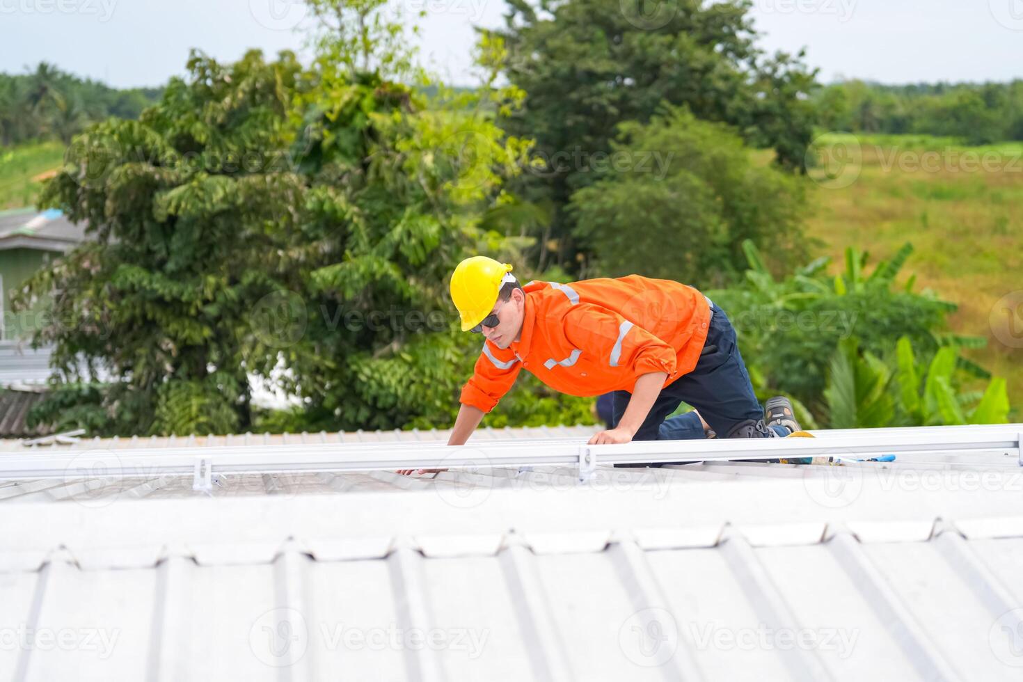 A man in an orange shirt and hard hat on the roof photo