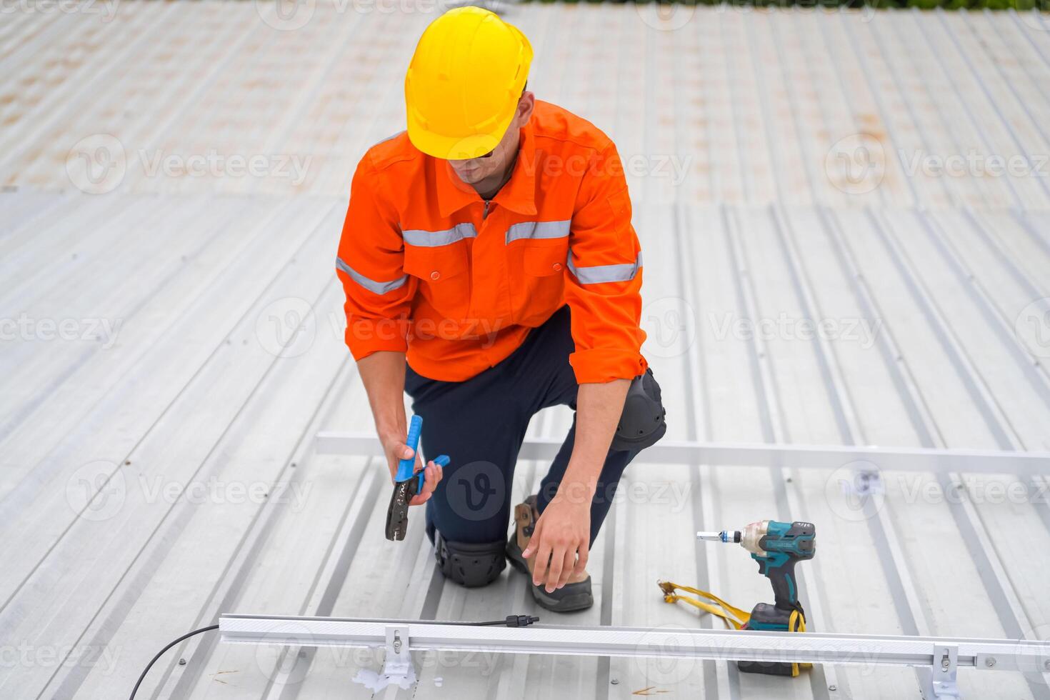 A man in an orange shirt and hard hat working on a roof photo