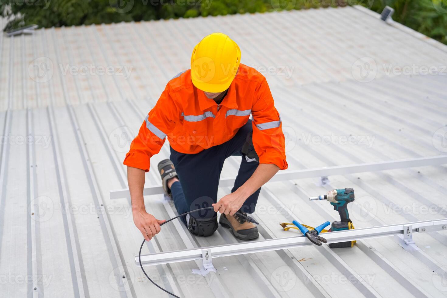 A man in an orange shirt and hard hat working on a roof photo