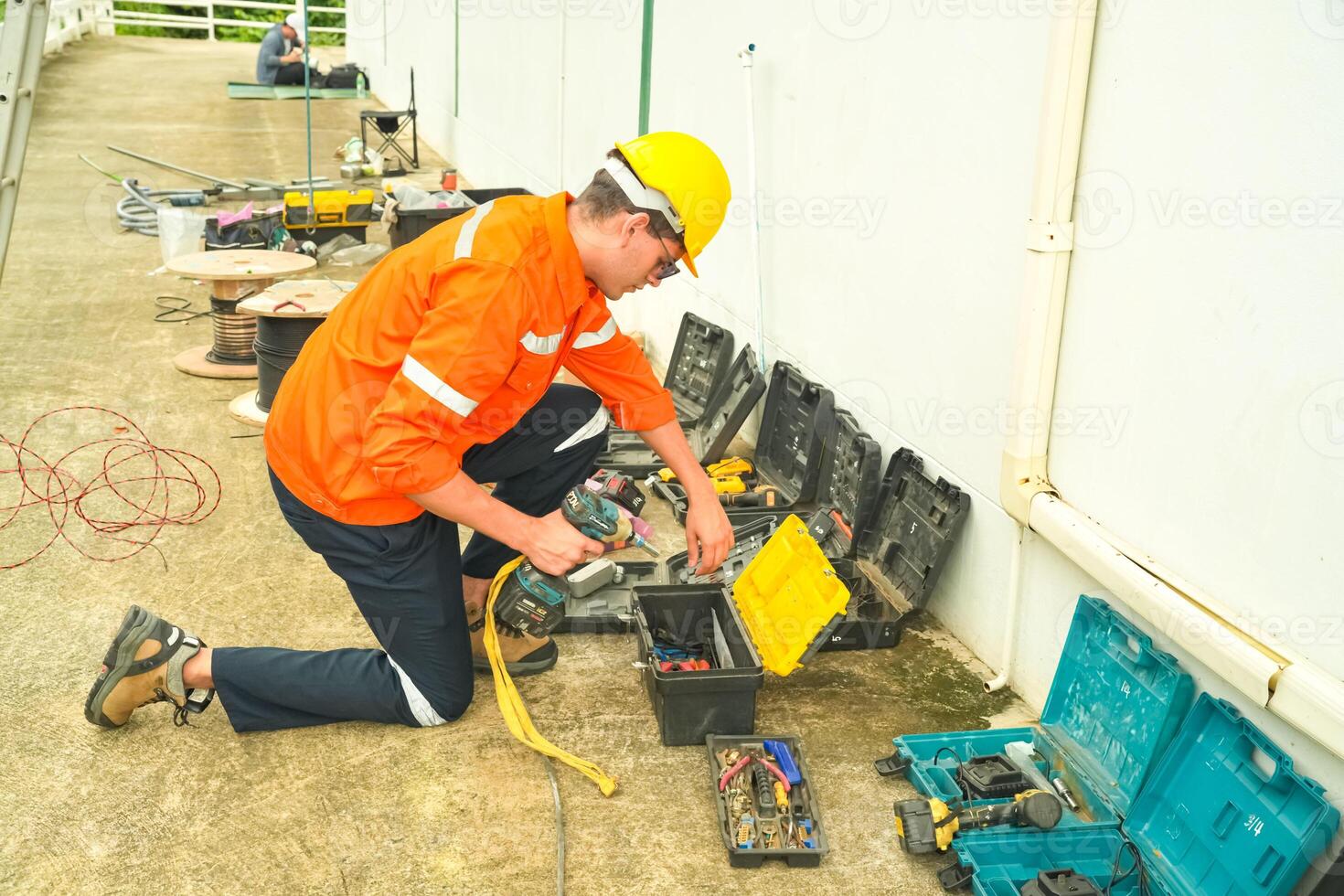 A man in an orange shirt and hard hat working on electrical equipment photo