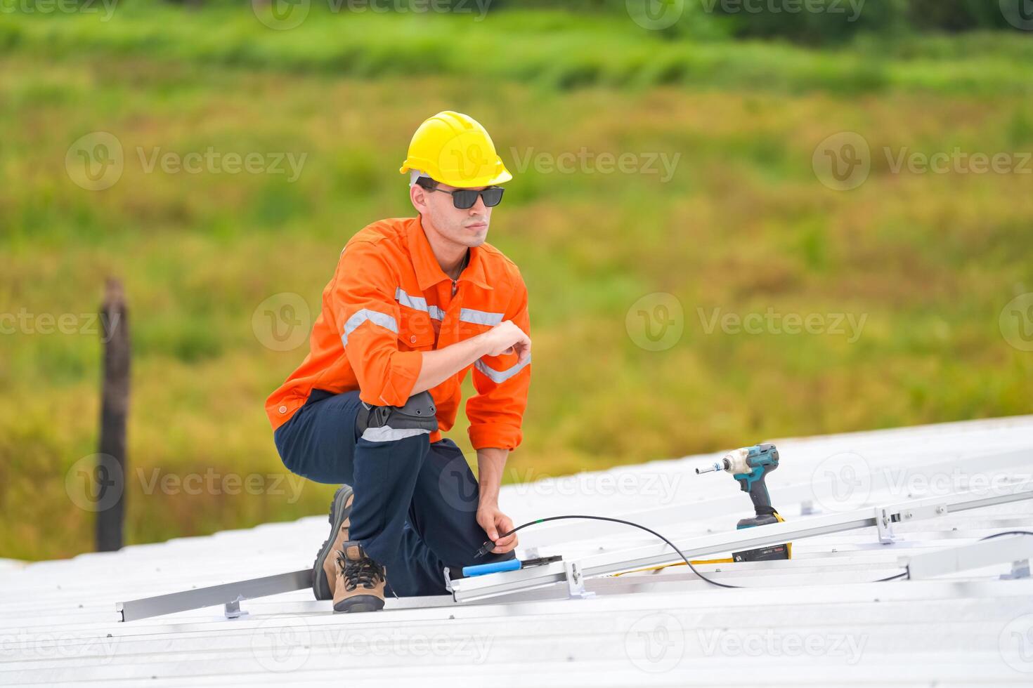 A man in an orange shirt and yellow hat working on a solar panel photo