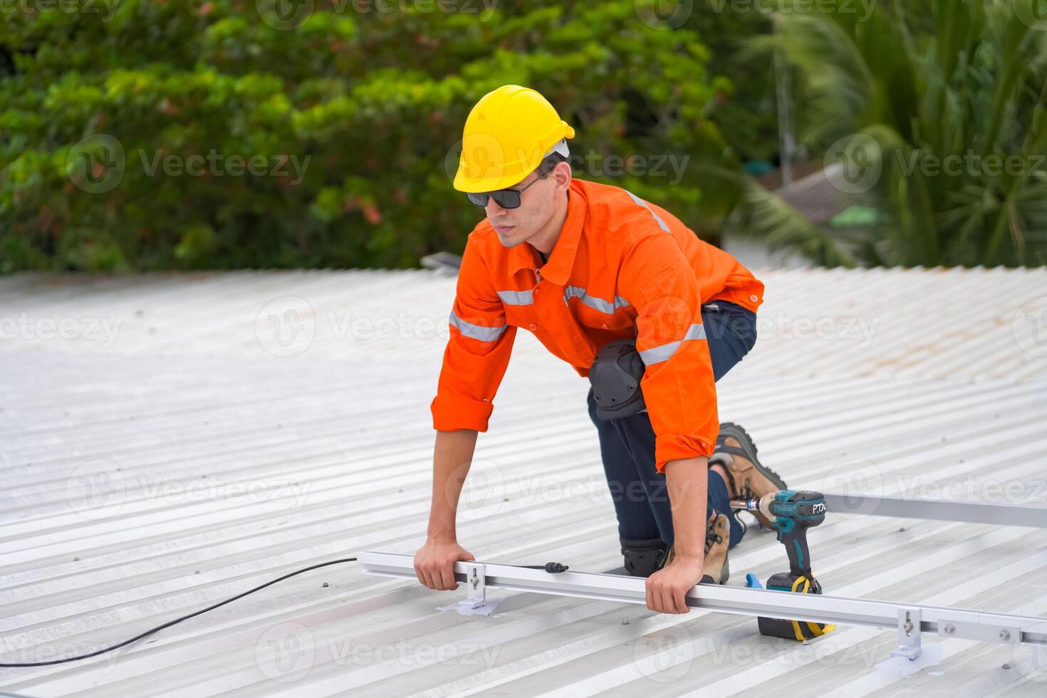 A man in an orange shirt and hard hat is working on a roof photo