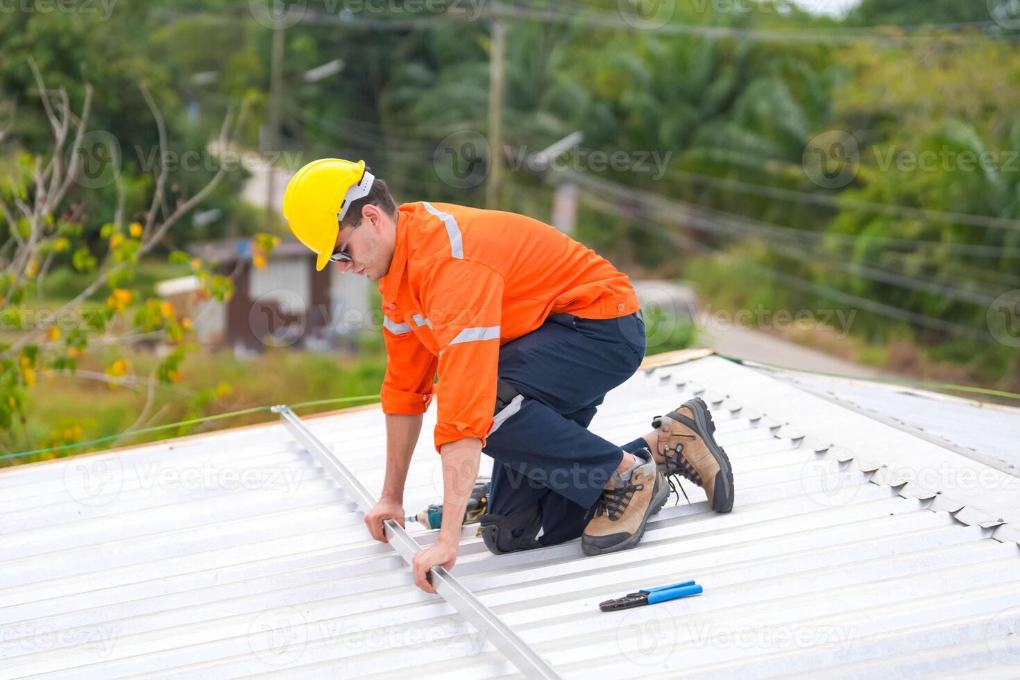 A man in an orange shirt and hard hat working on a roof photo