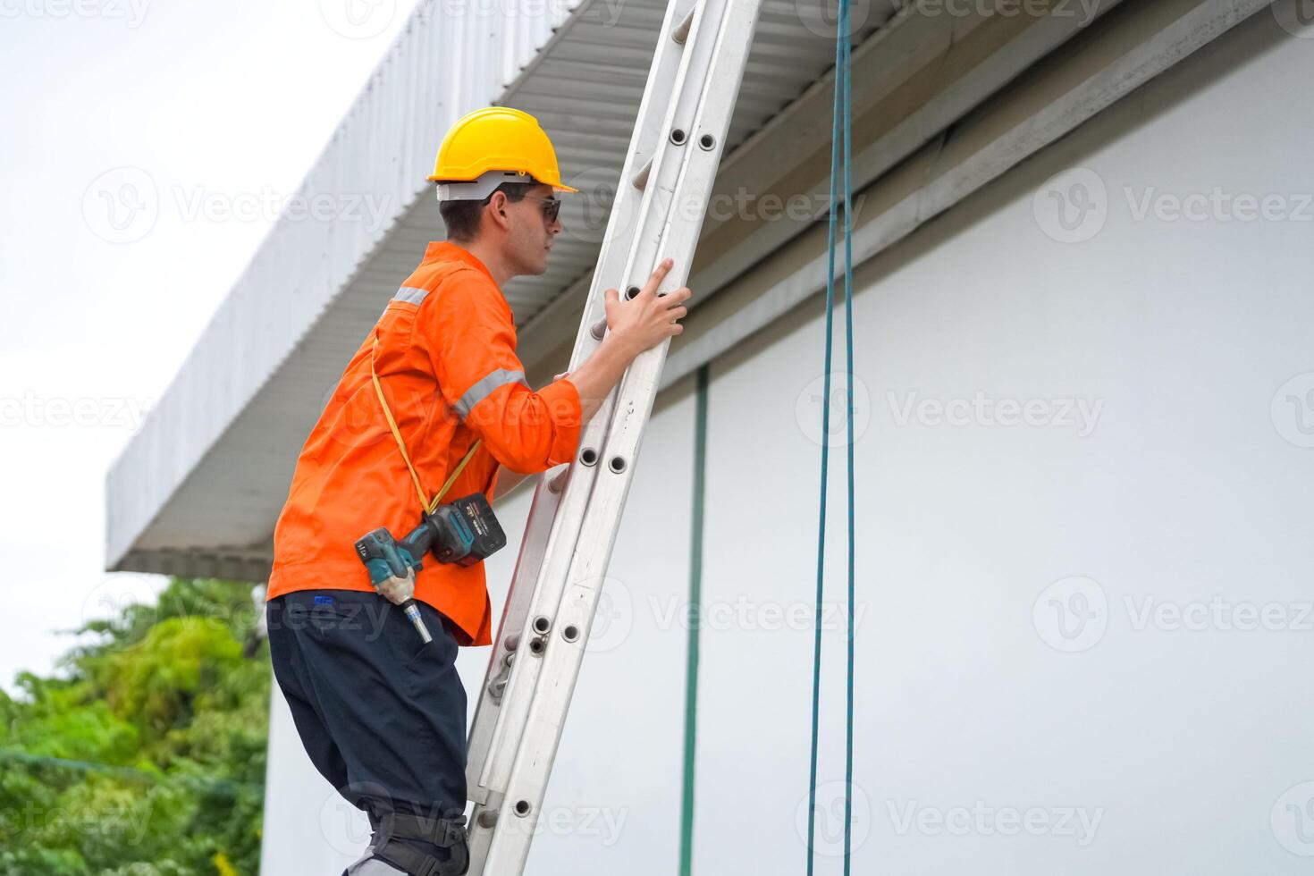 A man in an orange shirt and hard hat is climbing up a ladder photo