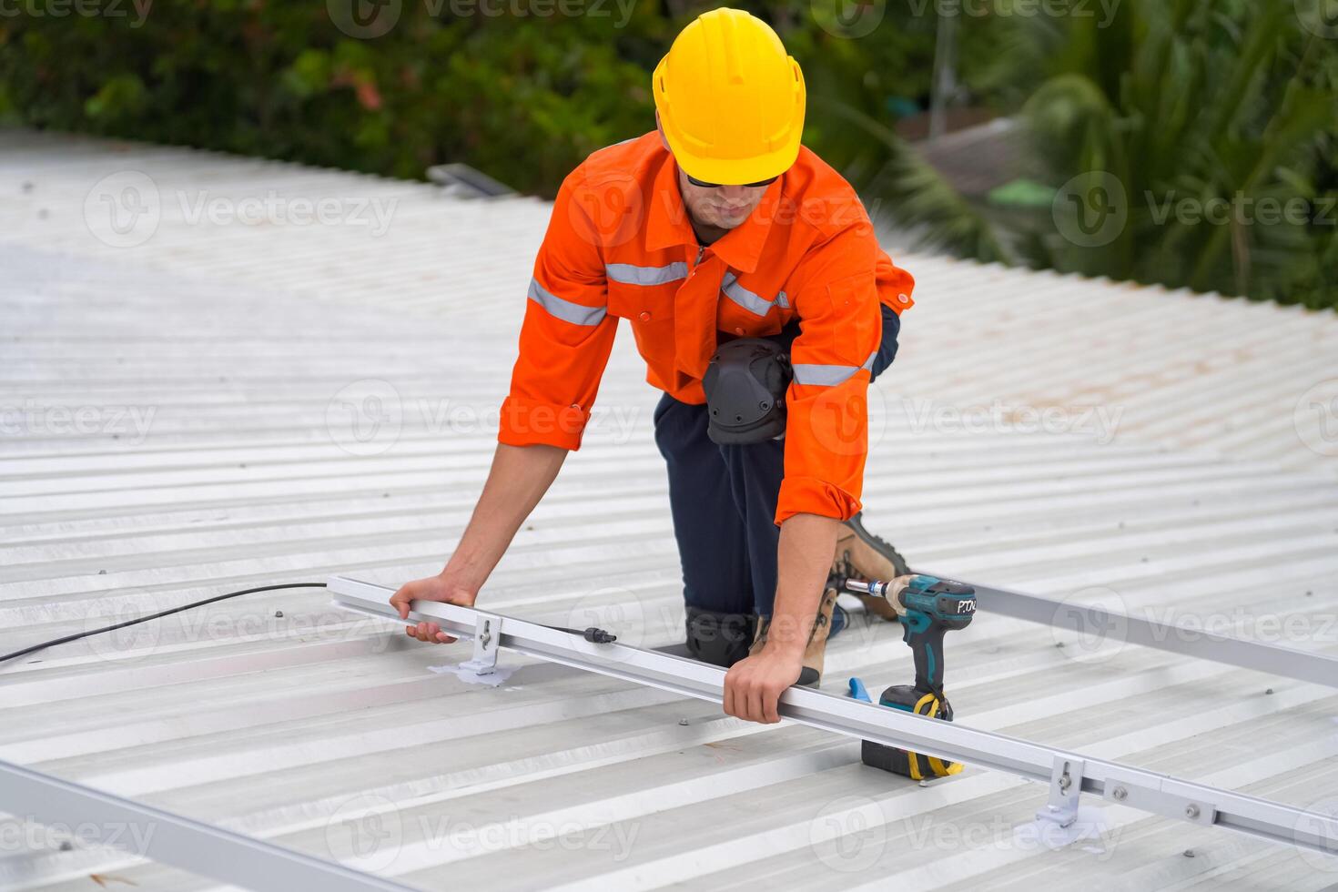 A man in an orange shirt and hard hat working on a roof photo