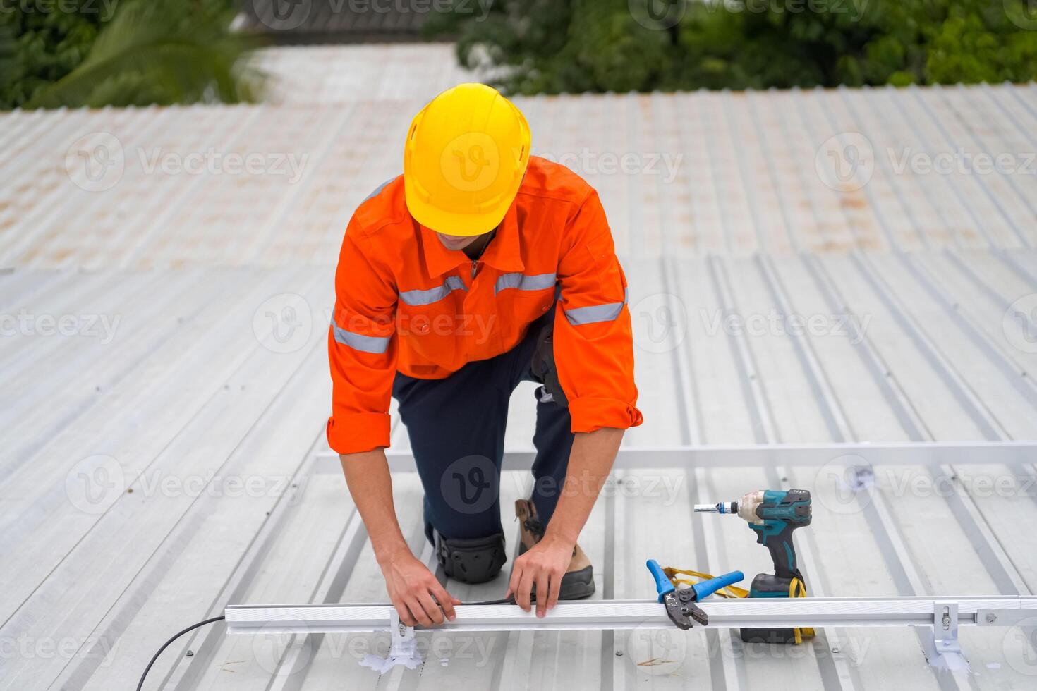 A man in an orange shirt and hard hat working on a metal roof photo