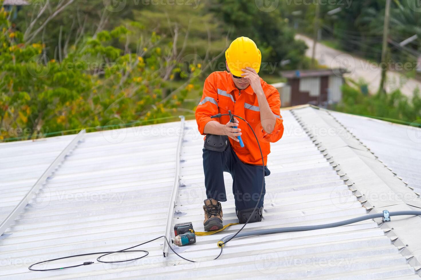 A man in an orange shirt and hard hat sitting on the roof photo