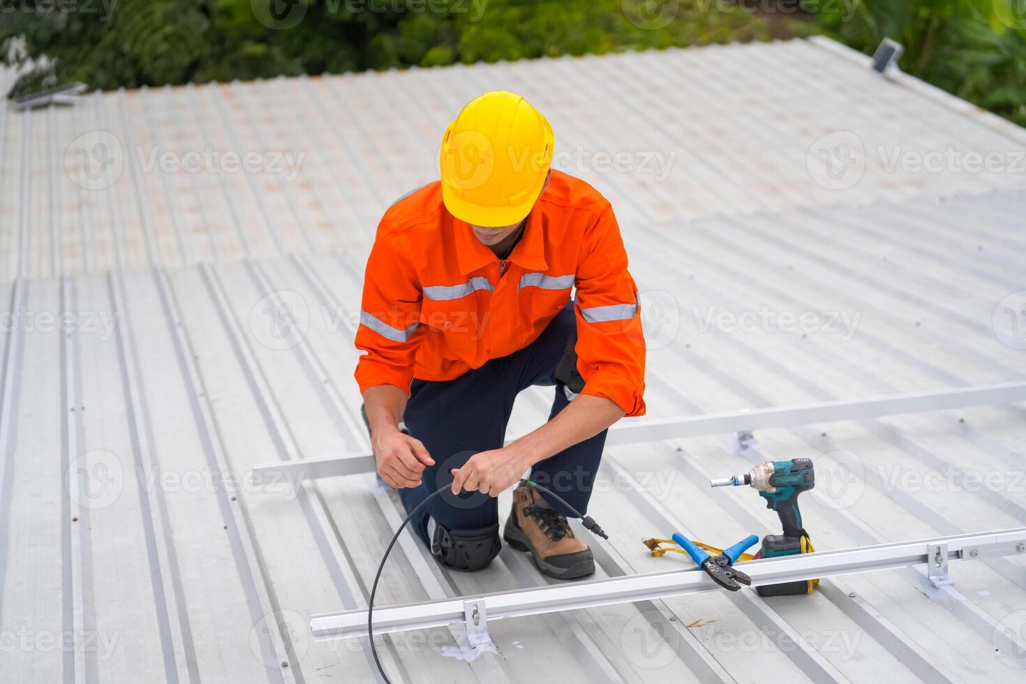 A man in an orange shirt and hard hat working on a roof photo