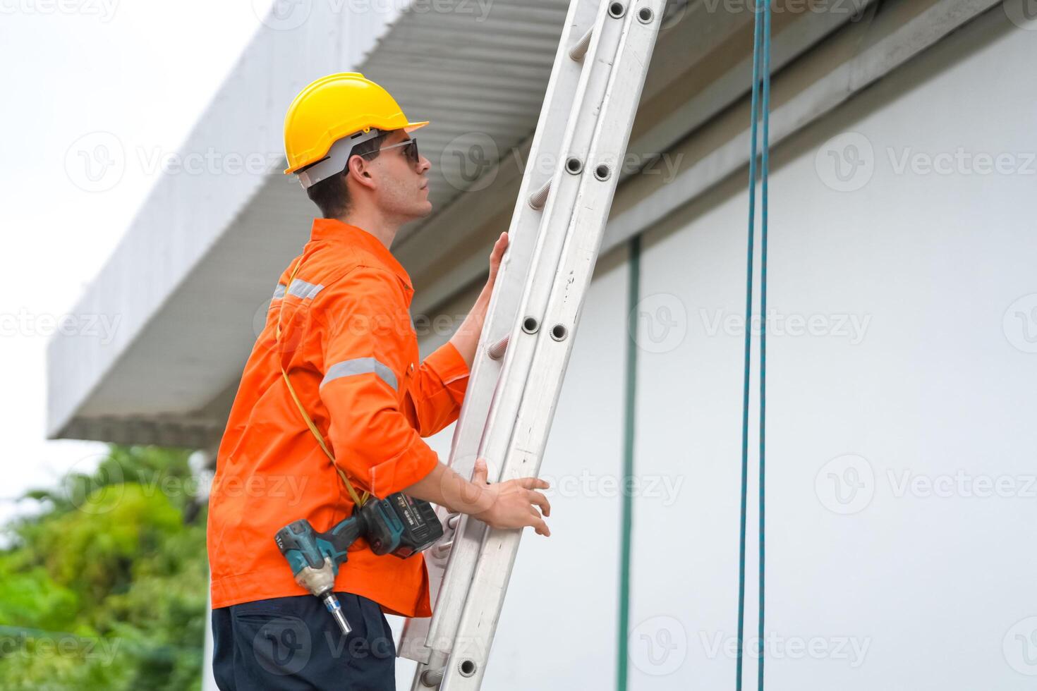 A man in an orange shirt and hard hat is standing on a ladder photo