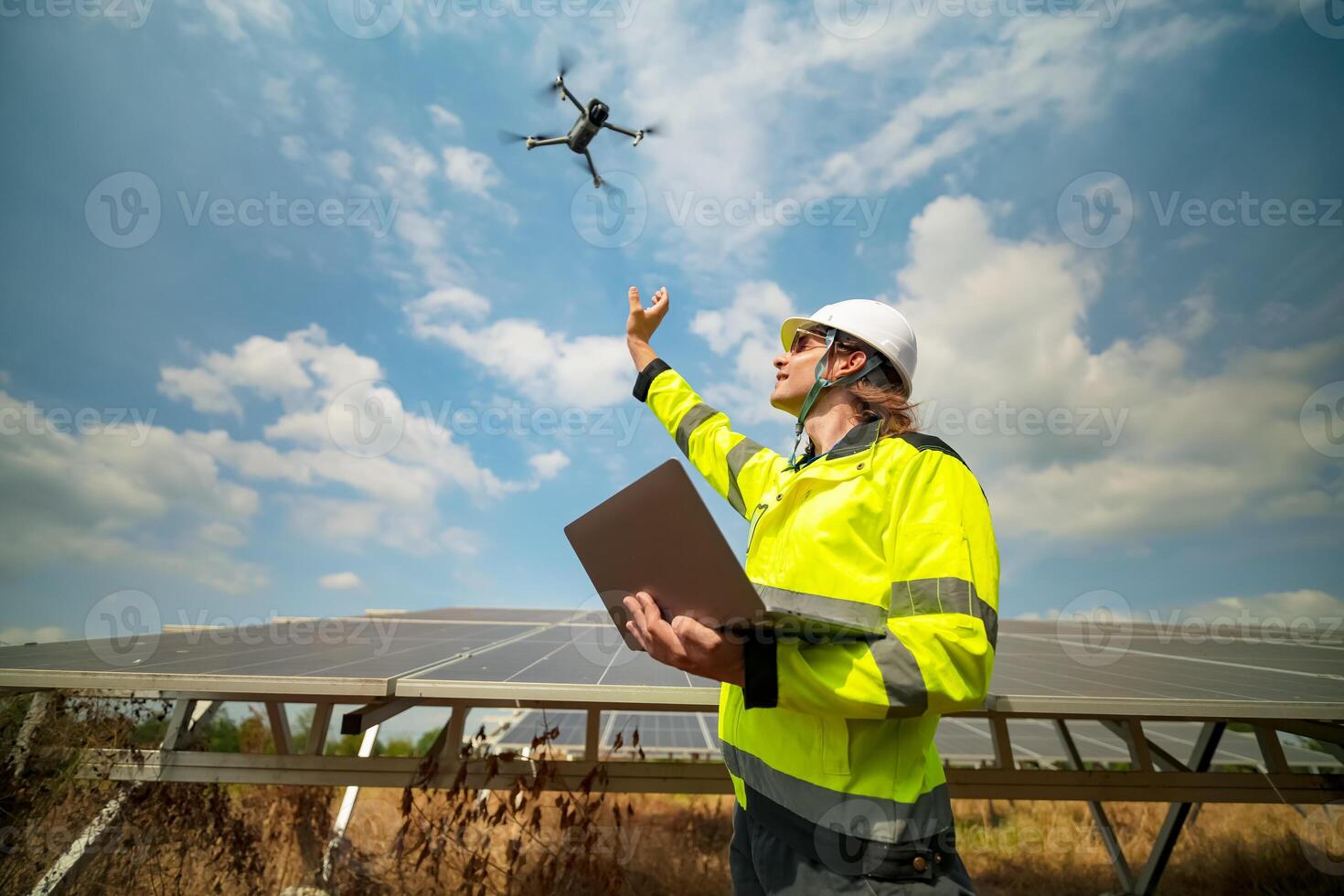 A man in a safety vest is holding a laptop and flying a drone photo