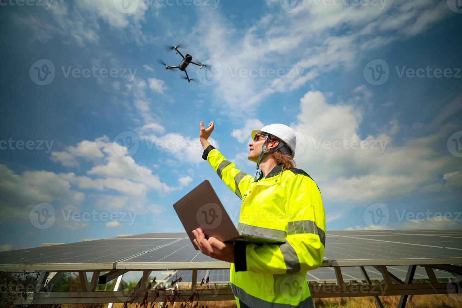 A man in a safety vest holding a laptop and flying a drone photo