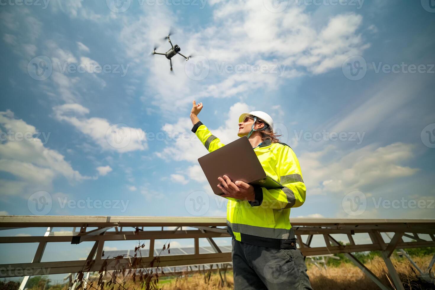 A man in a safety vest holding a laptop and flying a drone photo