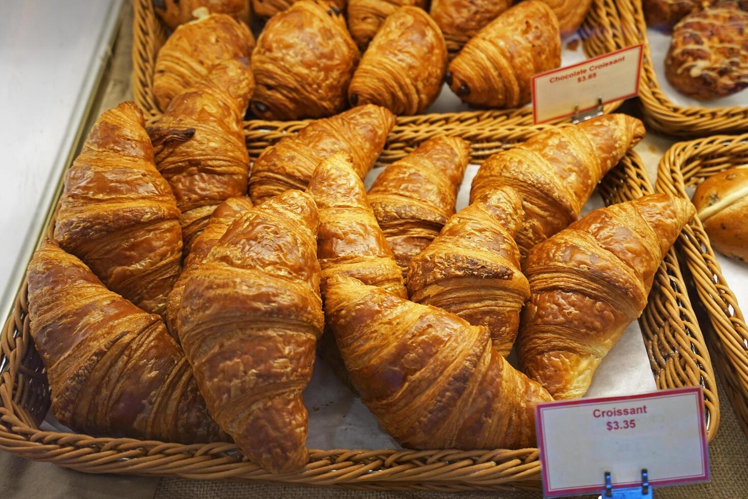 Baskets of plain butter, almond chocolate croissant, hot cross bun, ham and cheese Tiger claw, bacon and ham sandwiches, Kouign Amann and maple pull apart displayed in glass showcase box photo