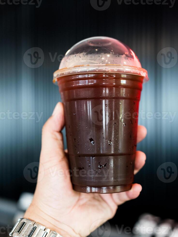 Man holding a plastic cup of iced Americano or black coffee photo