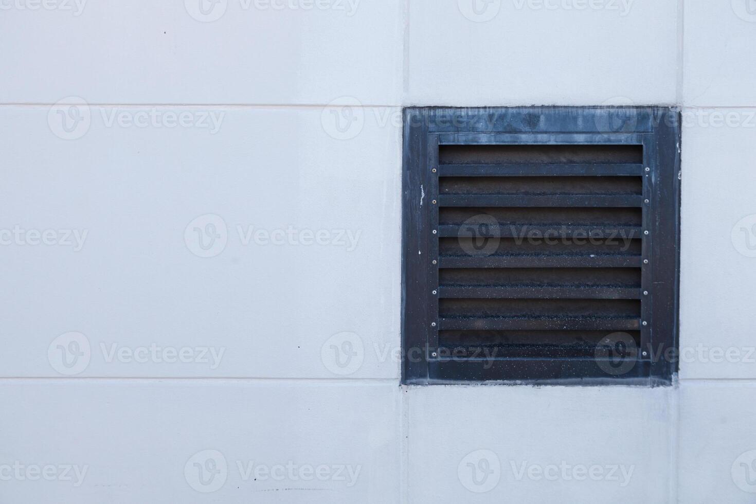 A window with a vent on the side of a white wall photo