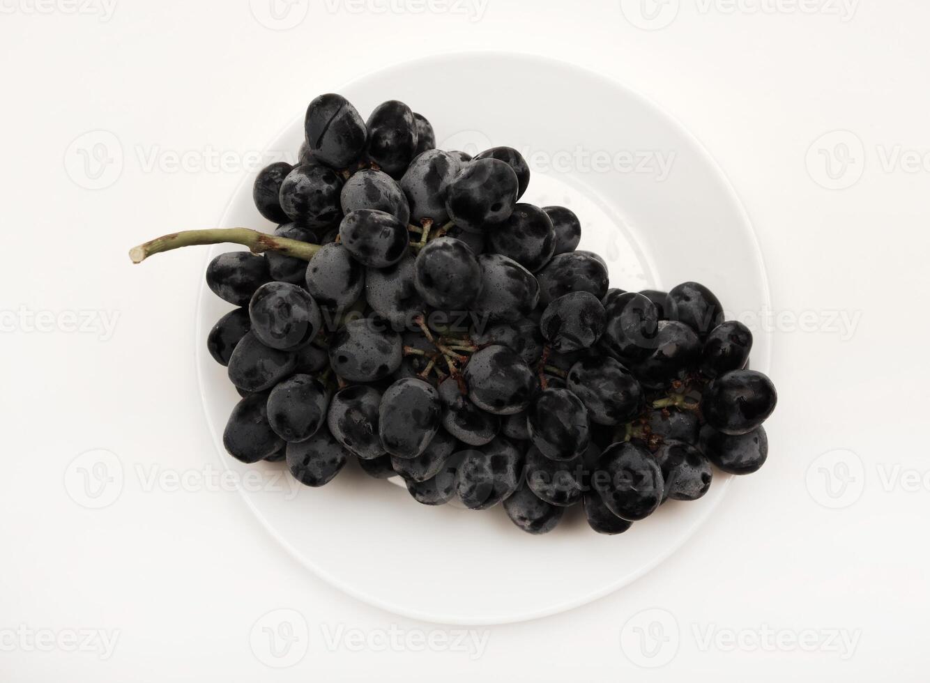 A branch of black grapes on a white plate. photo