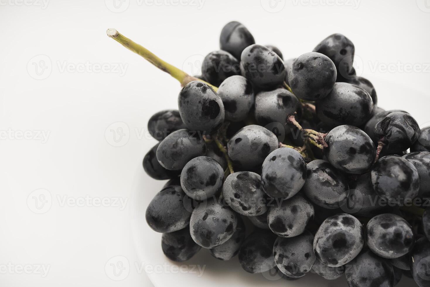 A branch of black grapes on a white plate. photo
