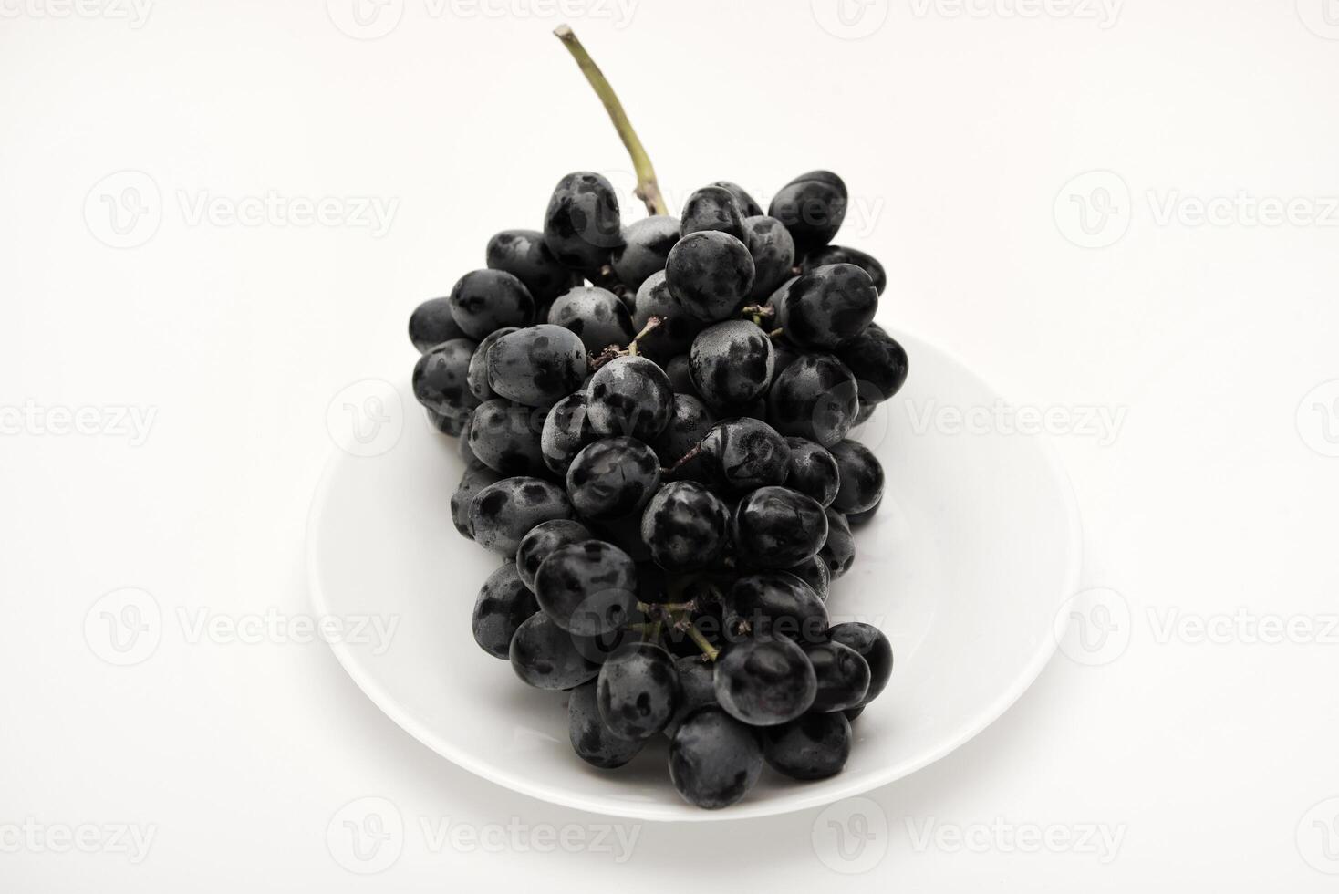 A branch of black grapes on a white plate. photo
