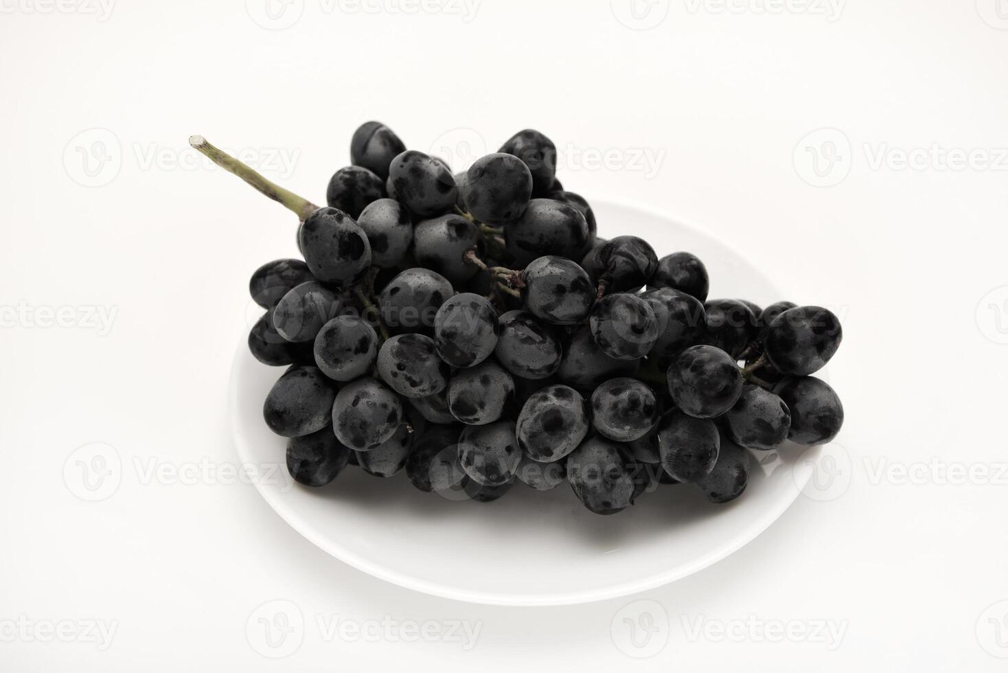 A branch of black grapes on a white plate. photo