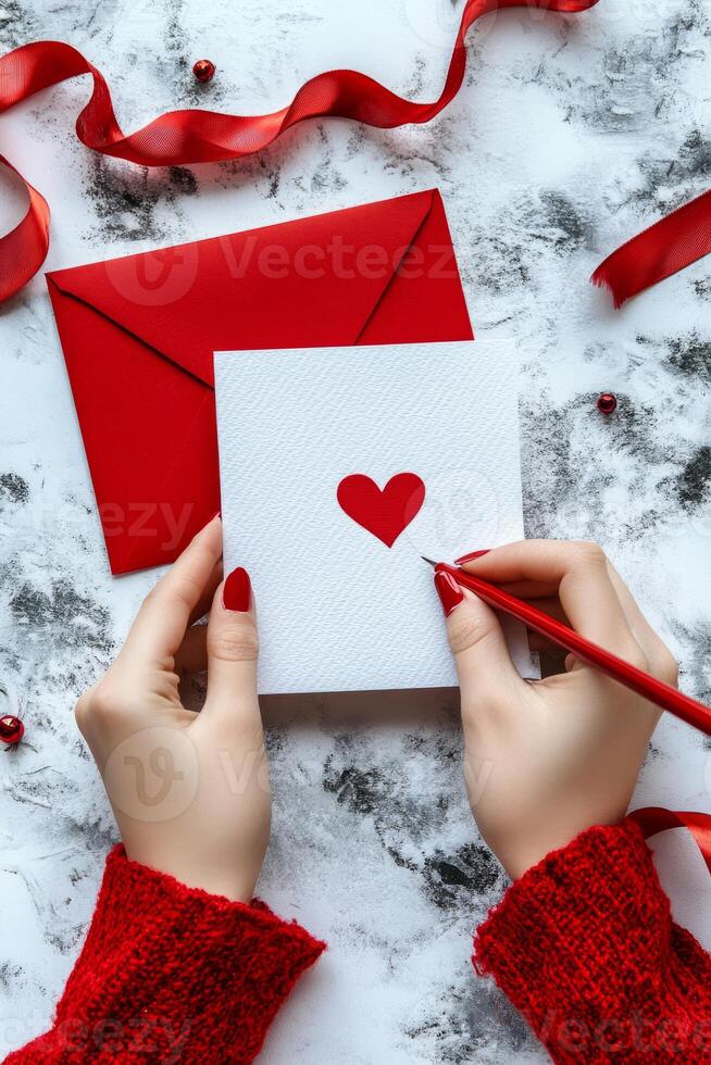 Hands creating message on a card with a red heart, surrounded by ribbon accents photo