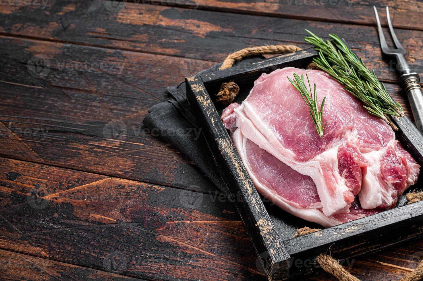Ready for cooking raw pork chop steaks in a wooden tray with rosemary. Wooden background. Top view. Copy space photo